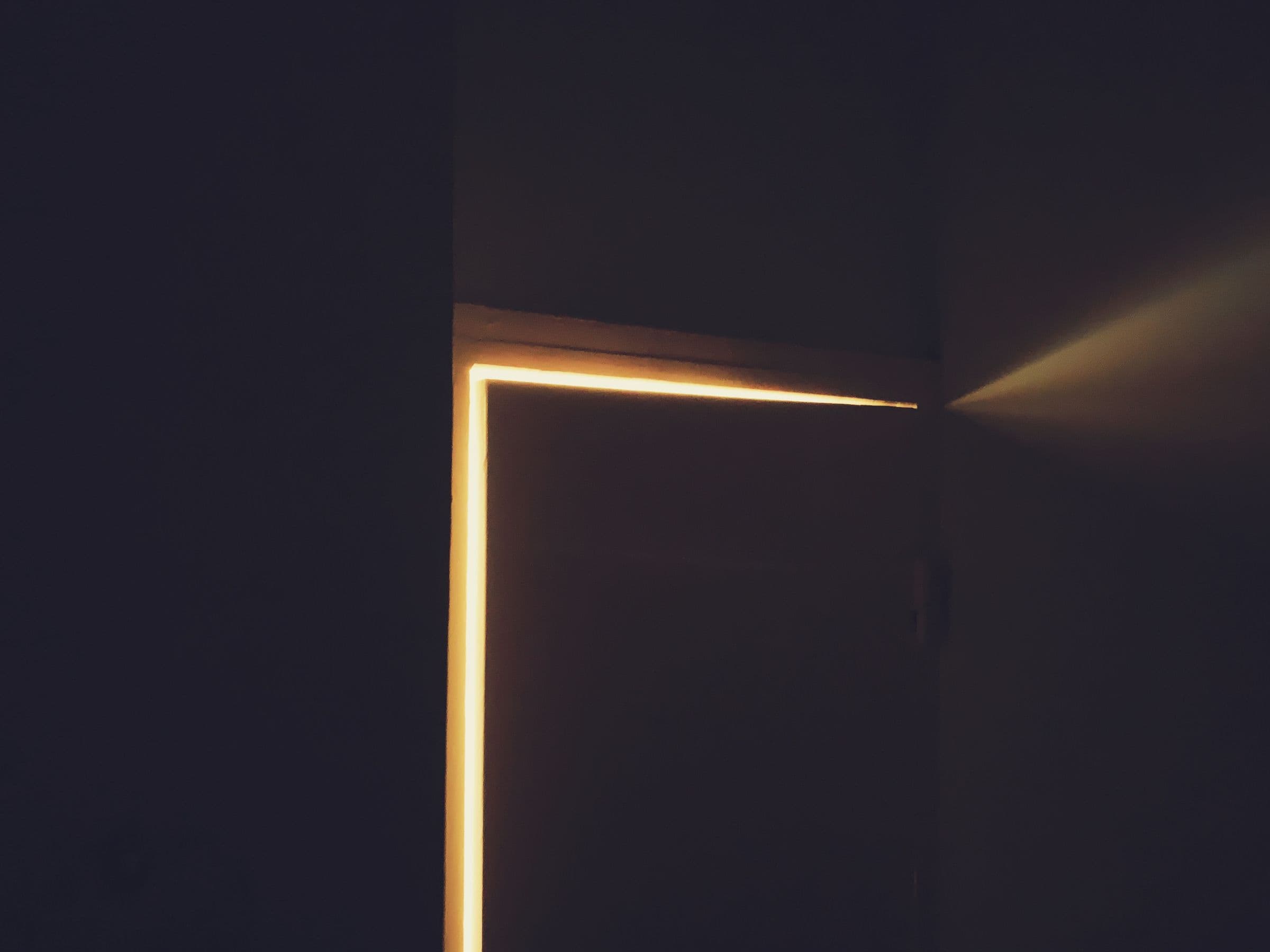 Warm light escaping through a slightly opened door into a dark room — evoking a vibe-coded application left quietly open to the world.